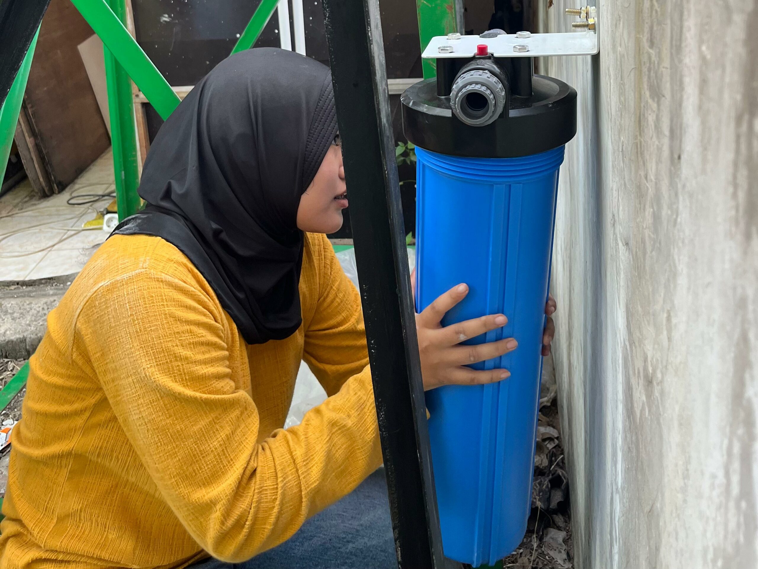 Salah satu anggota tim KKN saat memasang filter air untuk penyaring kotoran dari penampungan air hujan